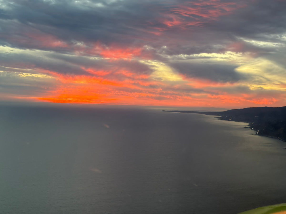 Aerial view of the coastline and mountains running along a calm ocean under a red and orange sunset