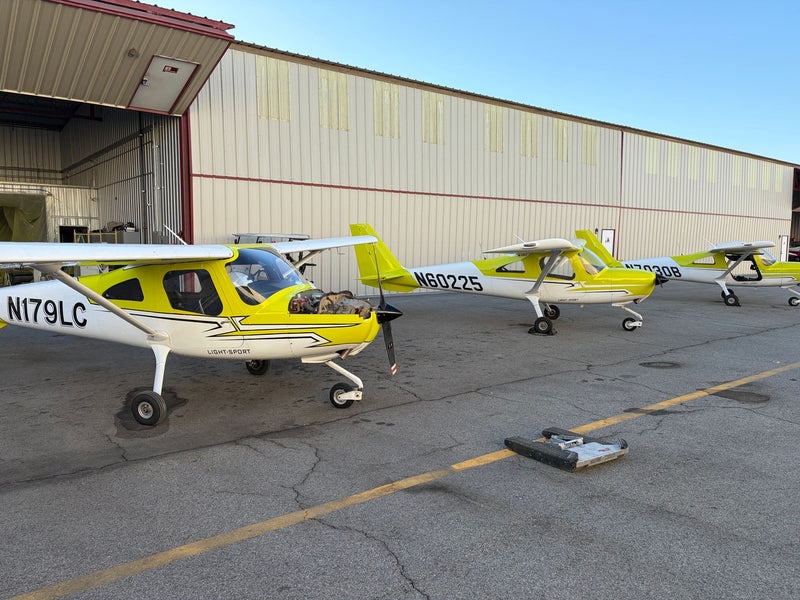 Yellow and white Cessna 162 trainers, N7030B among them, parked nose-out by a hangar at Van Nuys