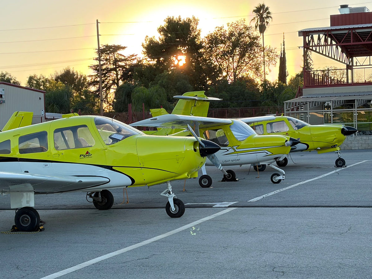 Yellow Piper and Cessna 162 trainers lined up on the ramp as the sun sets behind trees at Van Nuys