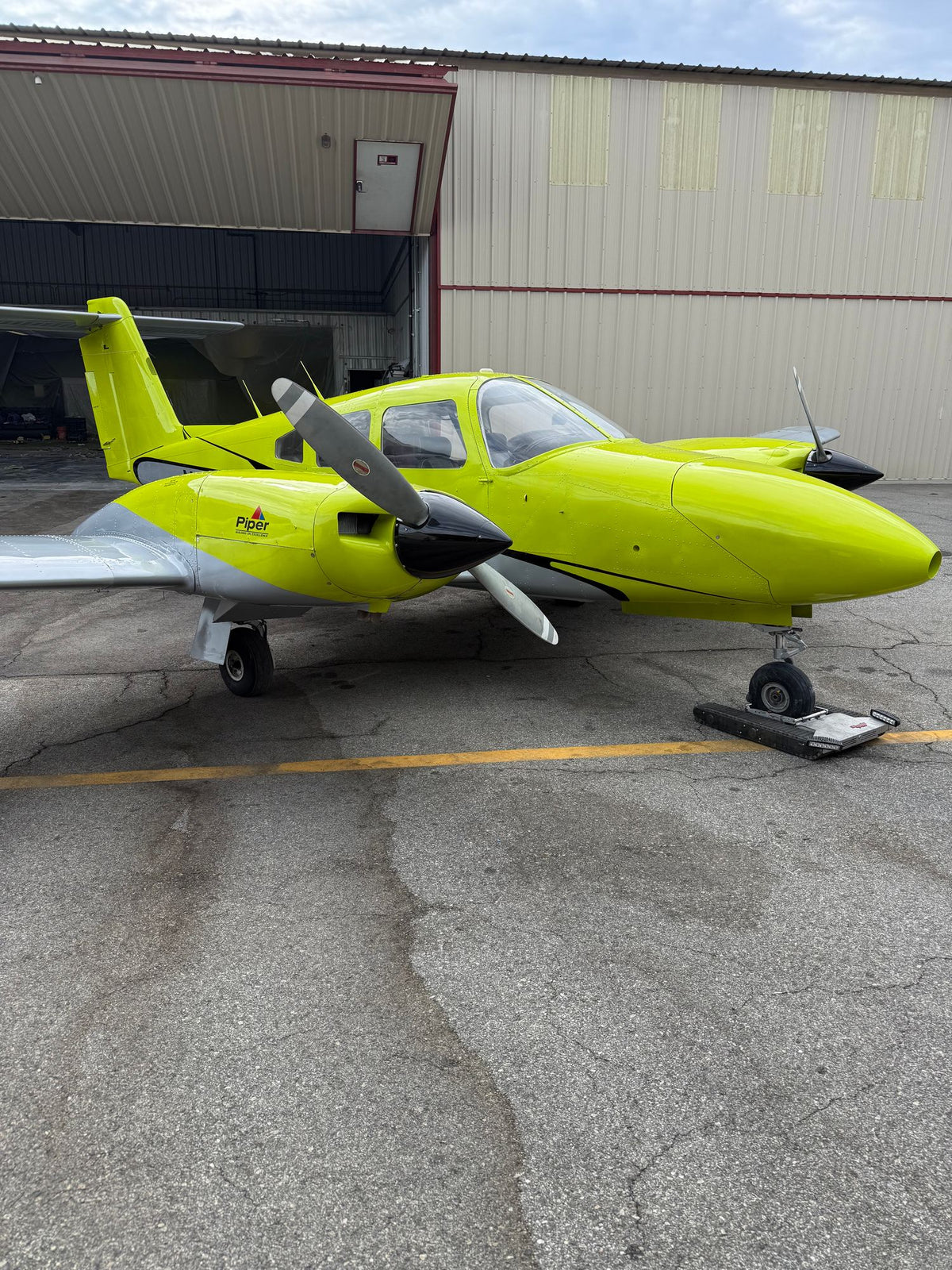 Yellow Piper Seminole twin parked in front of an open hangar door at Van Nuys Airport