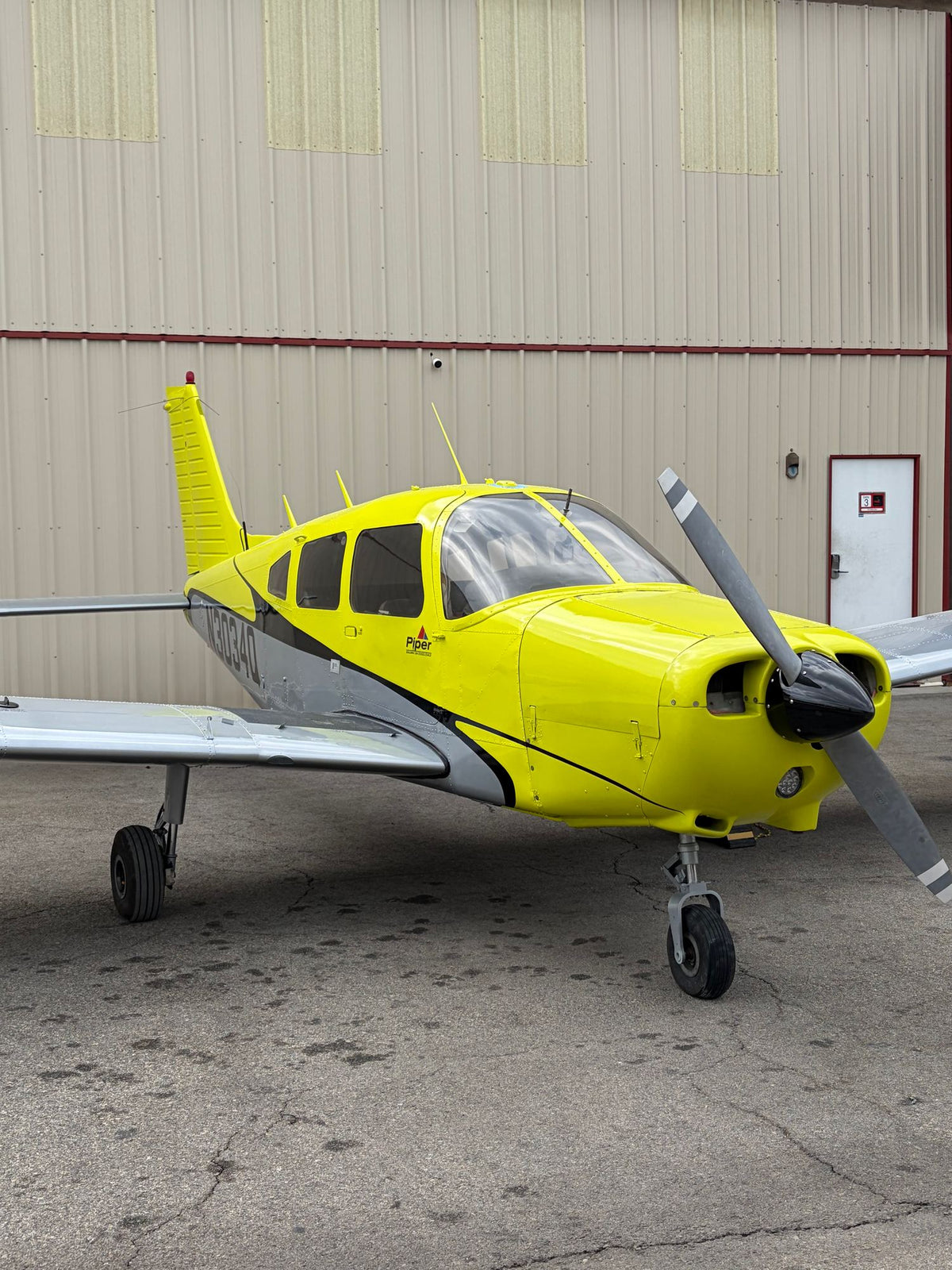 Yellow Piper Warrior parked in front of a tan hangar wall with a white door at Van Nuys