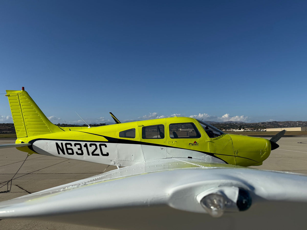 Wingtip navigation light in the foreground with yellow Piper Warrior N6312C behind on a sunny ramp