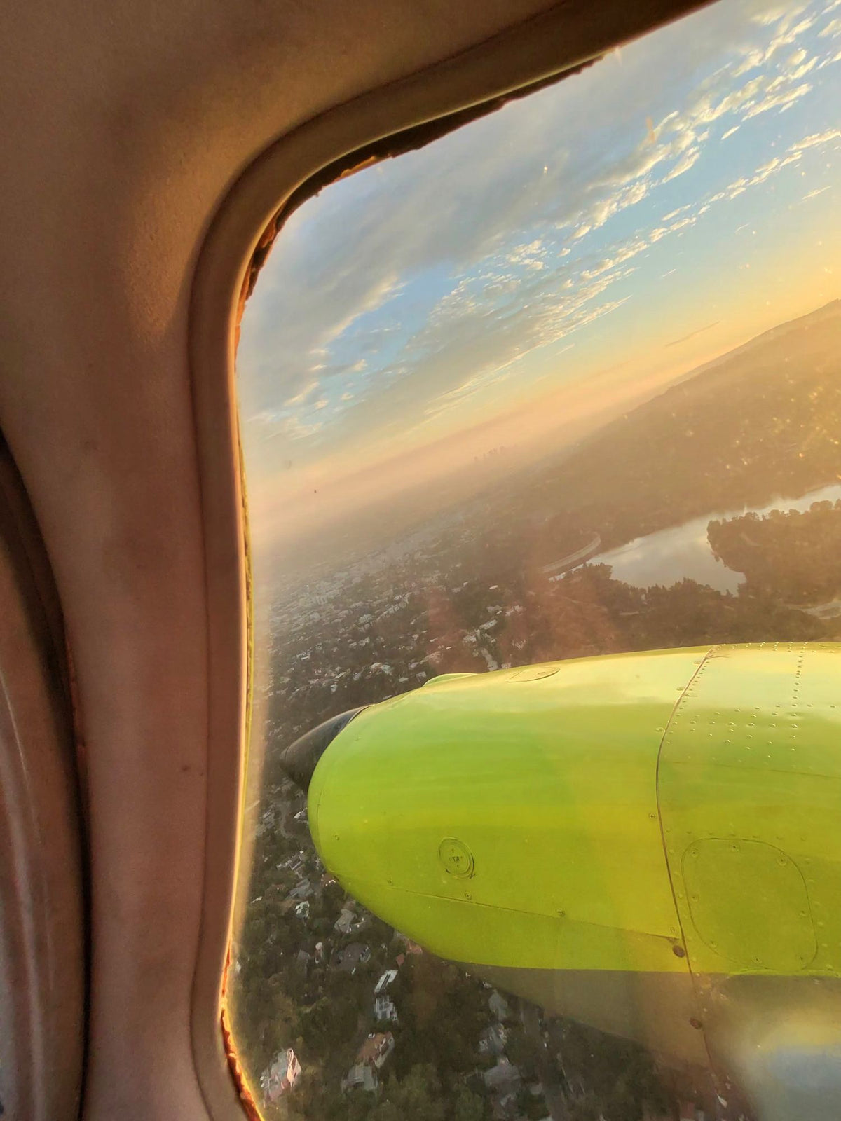View through a cabin window of a yellow engine nacelle with hillside neighborhoods and a reservoir far below