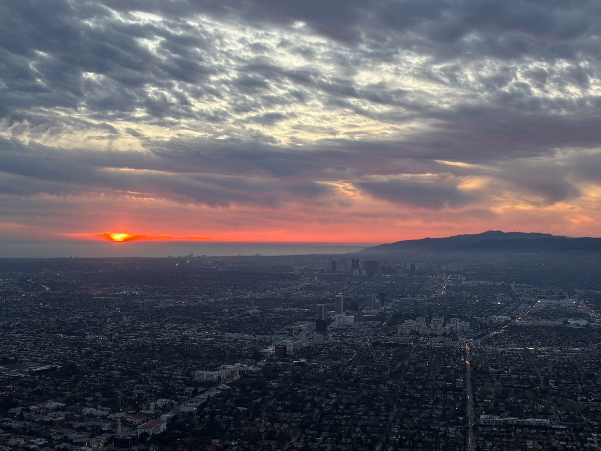 Aerial sunset over West Los Angeles with Century City towers, the Santa Monica Mountains and the ocean on the horizon