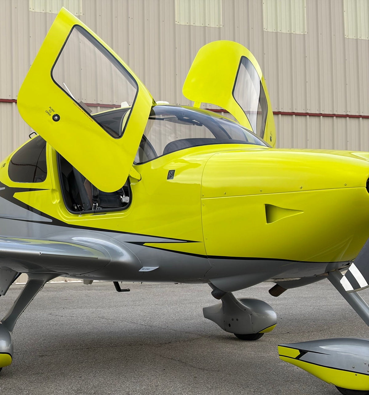Close view of a yellow Cirrus SR22 cowling, raised door and cabin with a hangar wall behind