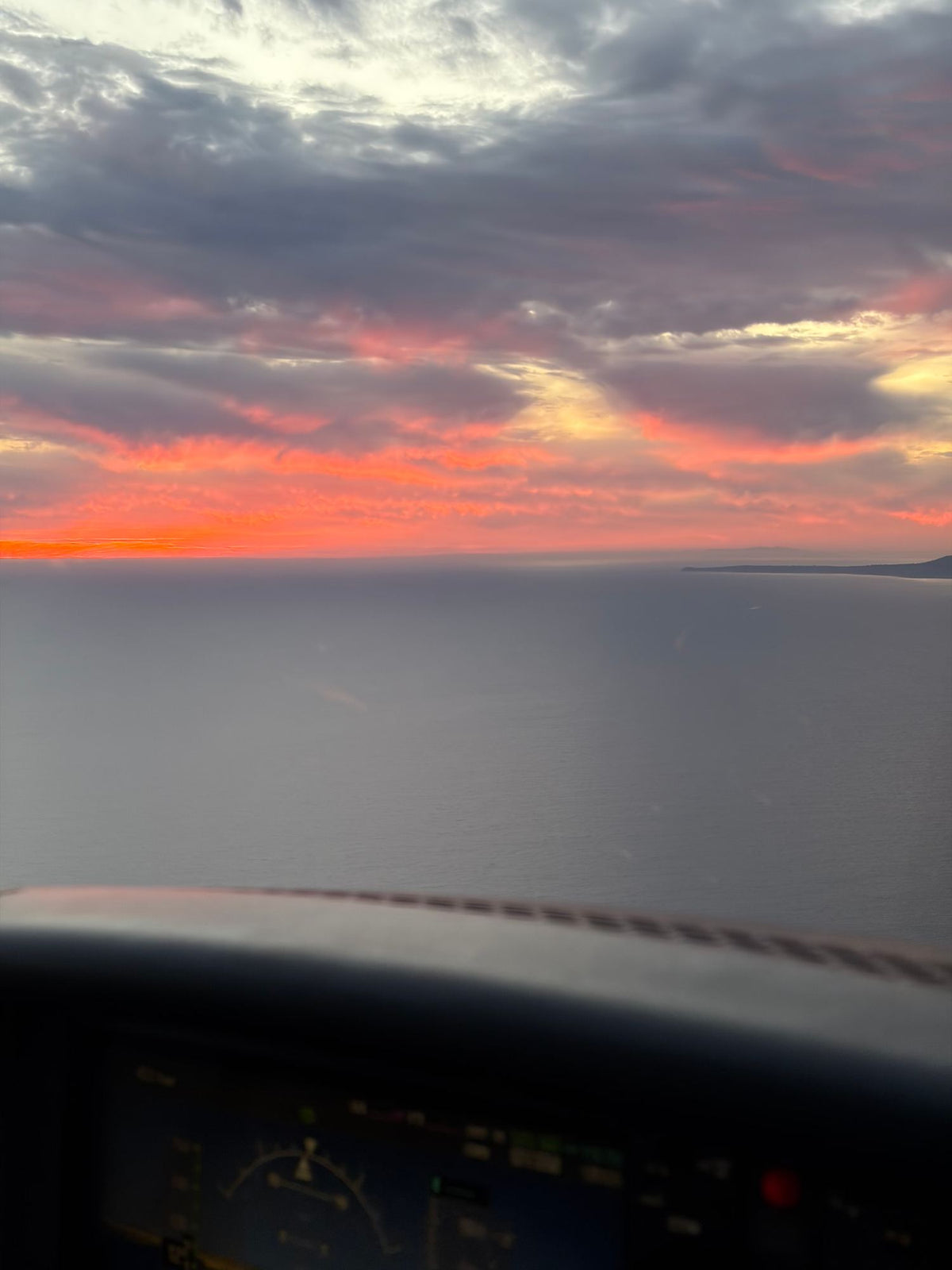 Red sunset over the Pacific seen above the dark glareshield of an aircraft instrument panel