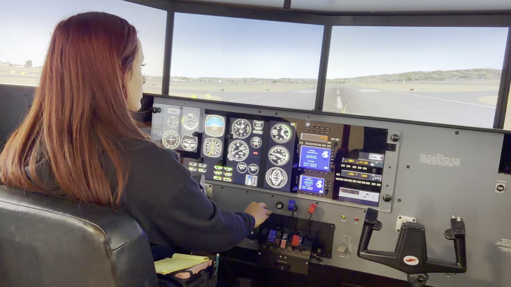 A student at the controls of the full-motion simulator with the runway on the screens ahead