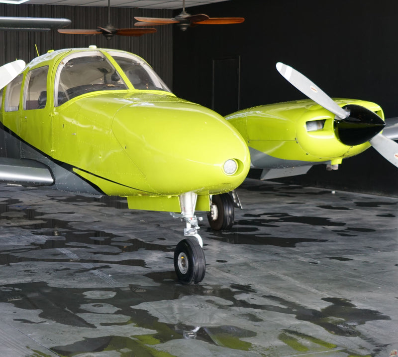 The nose and right engine of a yellow Piper Seminole in a dark hangar