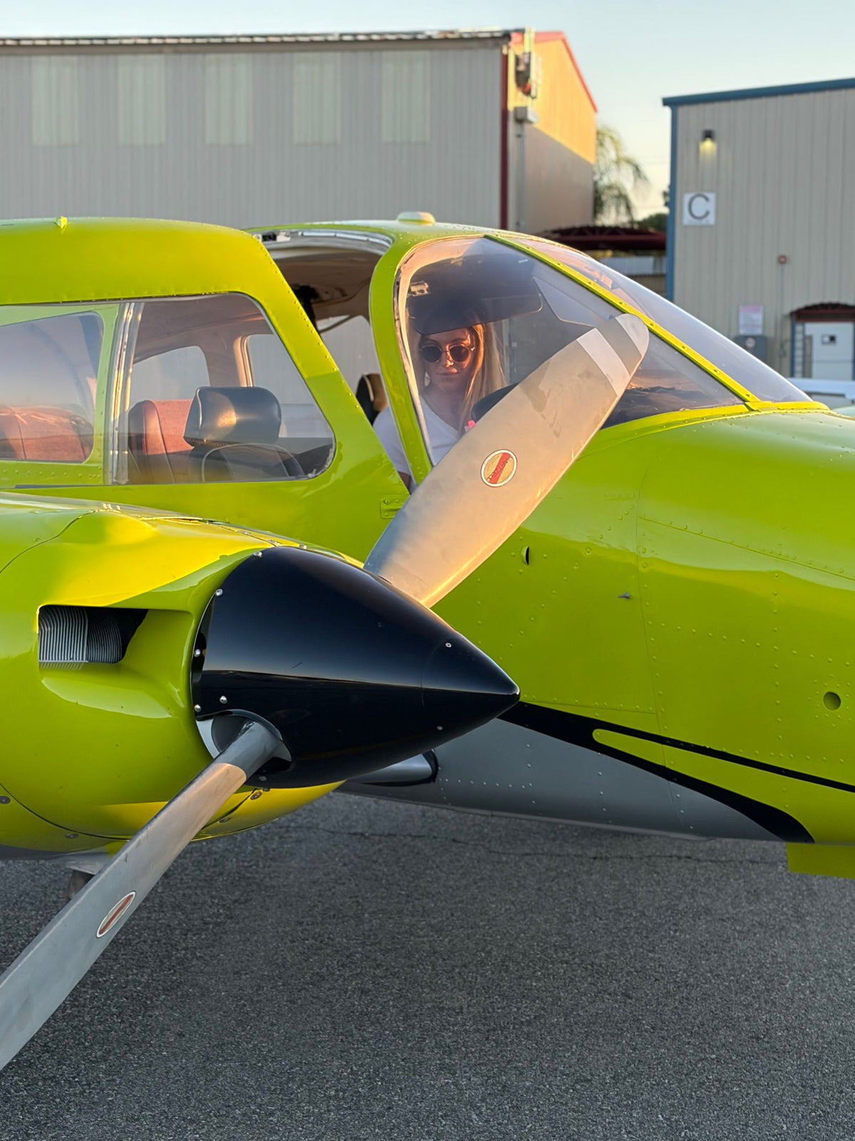 Pilot in sunglasses seated in the cockpit of a yellow Piper Seminole, seen past the left propeller