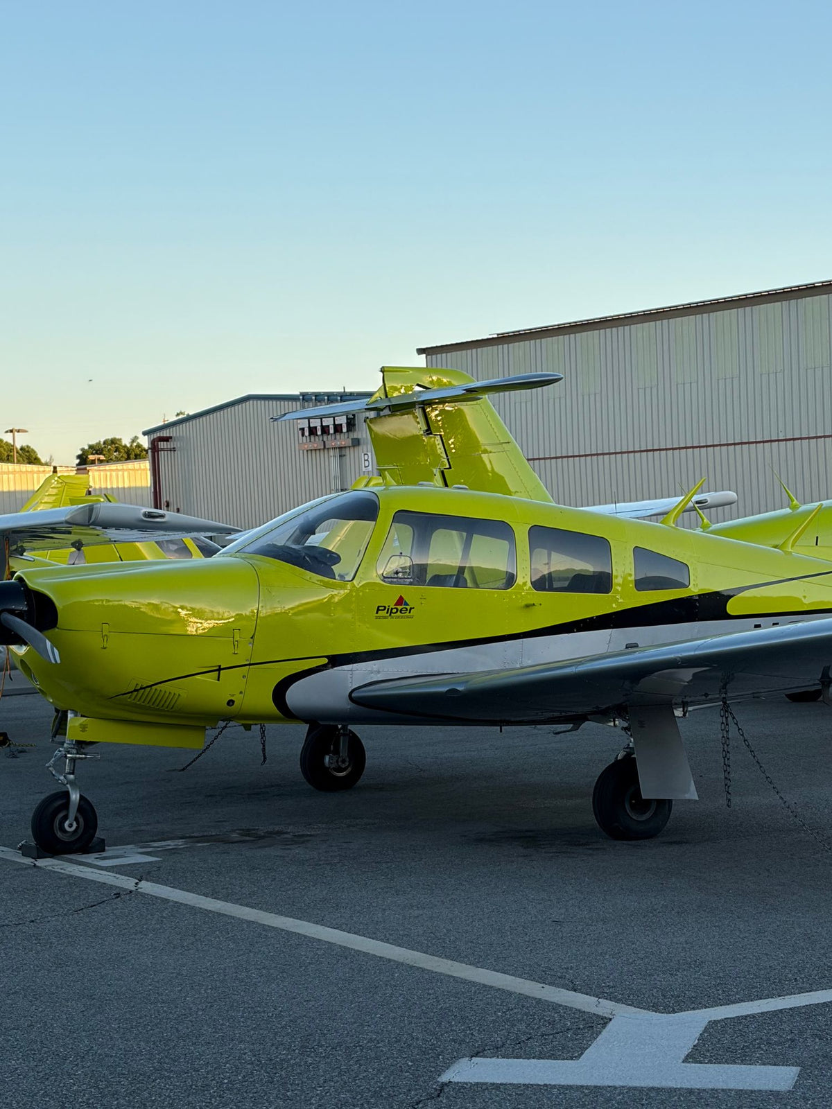 Yellow Piper trainer in the foreground with more yellow aircraft and hangars behind at dusk