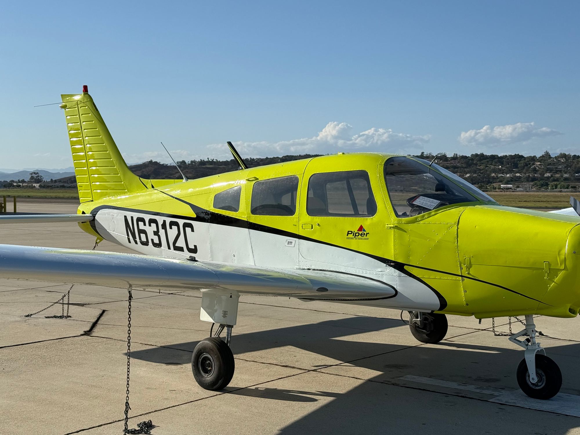Side view of Piper Warrior N6312C on a sunny ramp, cabin and cowling in view