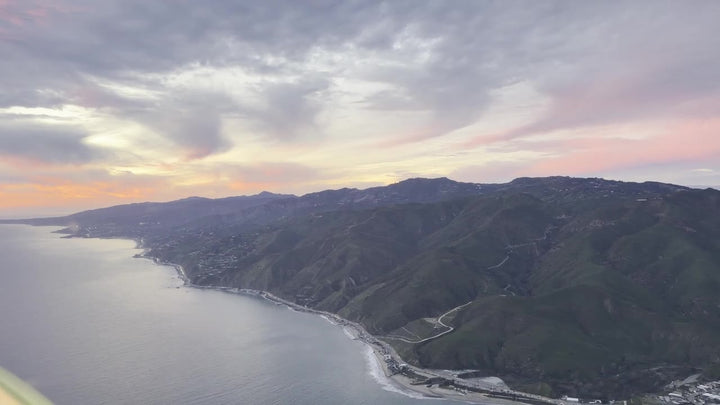 The Malibu coastline at sunset seen from a small airplane, the Santa Monica Mountains dropping into the Pacific Ocean with Pacific Coast Highway along the shore