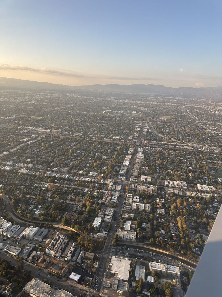 The San Fernando Valley seen over the wing of a small training airplane just after takeoff from Van Nuys Airport, with tree-lined streets and a long boulevard running toward the hills