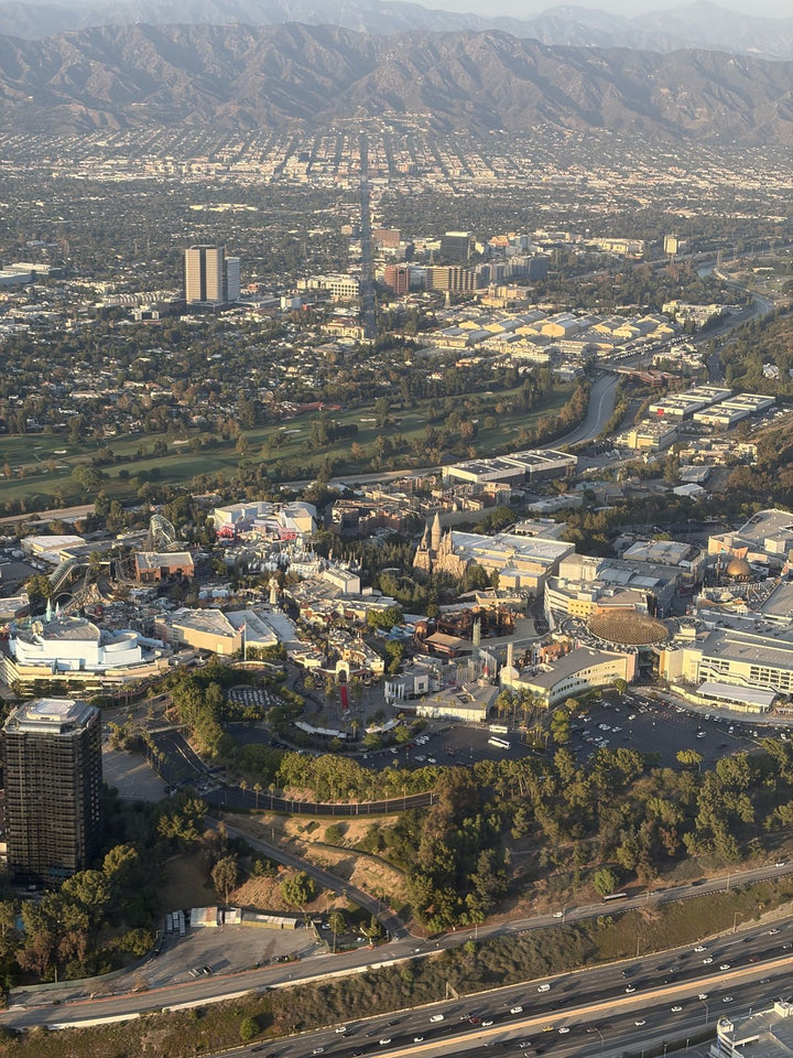 Universal Studios Hollywood seen from a small airplane, the theme park and studio soundstages on the hillside above the 101 freeway, with the Los Angeles River, Burbank and the Verdugo Mountains behind